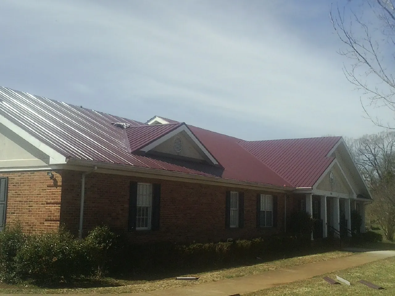 Red metal roof with gabled entries on a long brick building, from a Hail Damage Roof Repair job in Biloxi