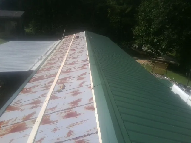 Old rusted panels beside newly installed green metal roofing — Wind Damage Roof Repair by Roofing Brothers in Biloxi
