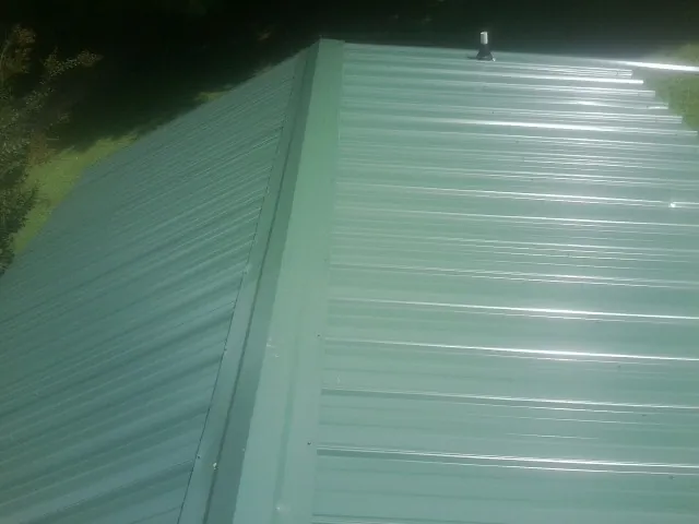 New green metal panels meeting at the ridge of a roof — Flat Roof Repair work by our crew in Biloxi