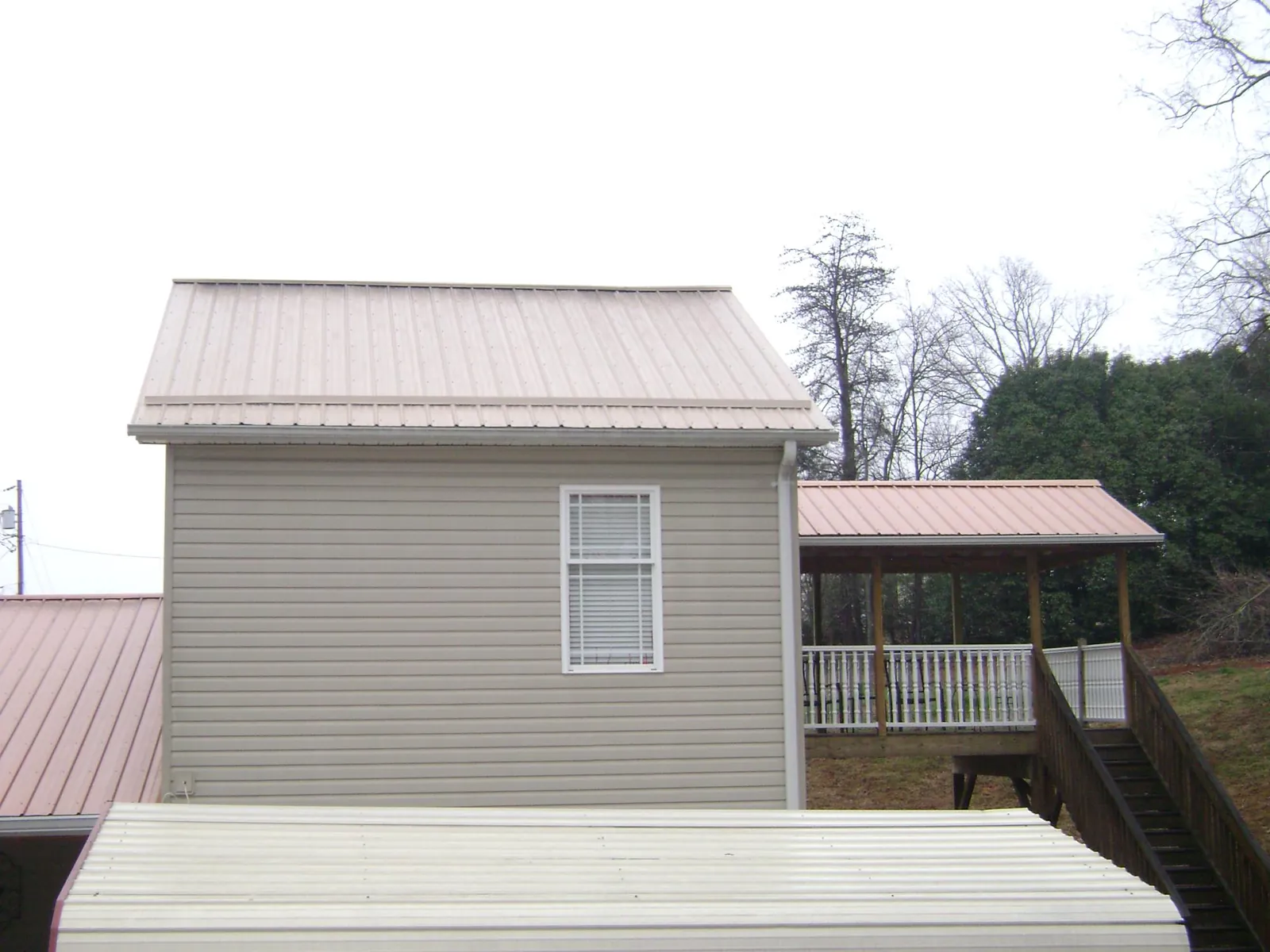 Tan metal roofs on a two story addition and attached porch, from a Roof Replacement job in Biloxi
